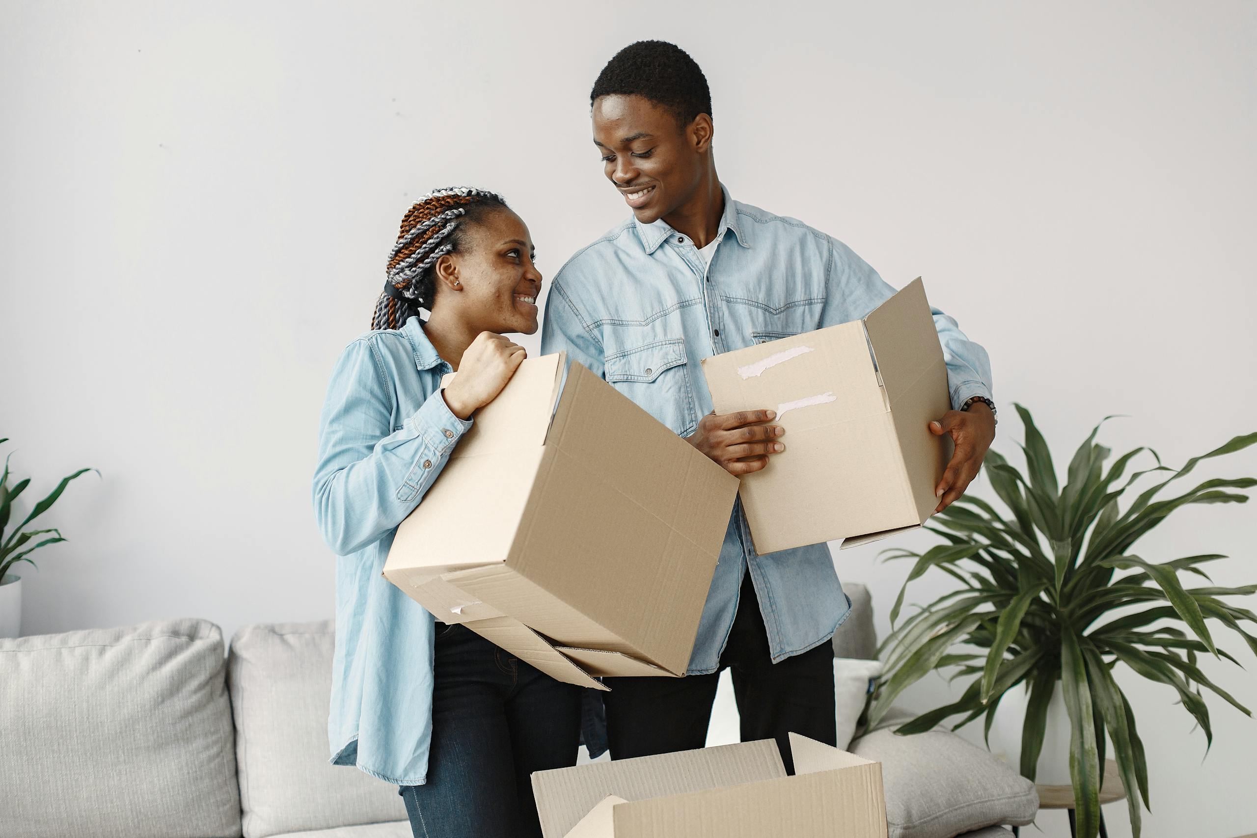 A smiling couple carrying cardboard boxes while moving indoors, capturing a joyful moment.